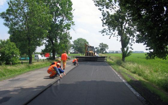 Rozkładanie kompozytu HaTelit® o szerokości 5,00 m na jezdni o szerokości 7,00 m, z jednoczesnym zrolowaniu części siatki zakrywającej drugi pas ruchu, po którym wahadłowo odbywał się ruchu pojazdów podczas wykonywania robót bitumicznych.